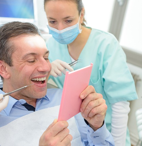 A man smiling at his new dental crown in a mirror