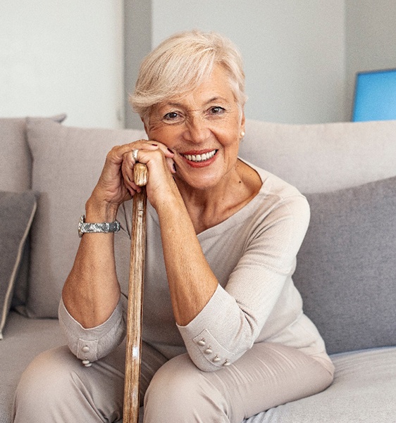 Woman in beige outfit on beige couch smiling leaning on walking cane