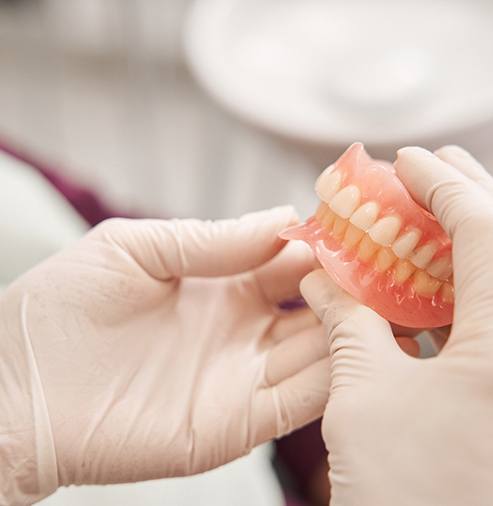 Gloved hands holding full set of dentures