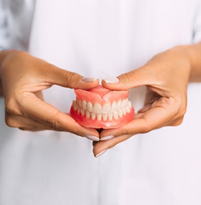 Hands holding full set of dentures in front of abdomen